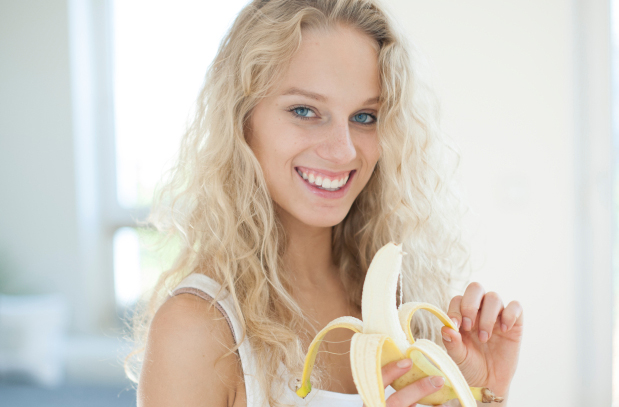 Portrait of young woman peeling banana in house